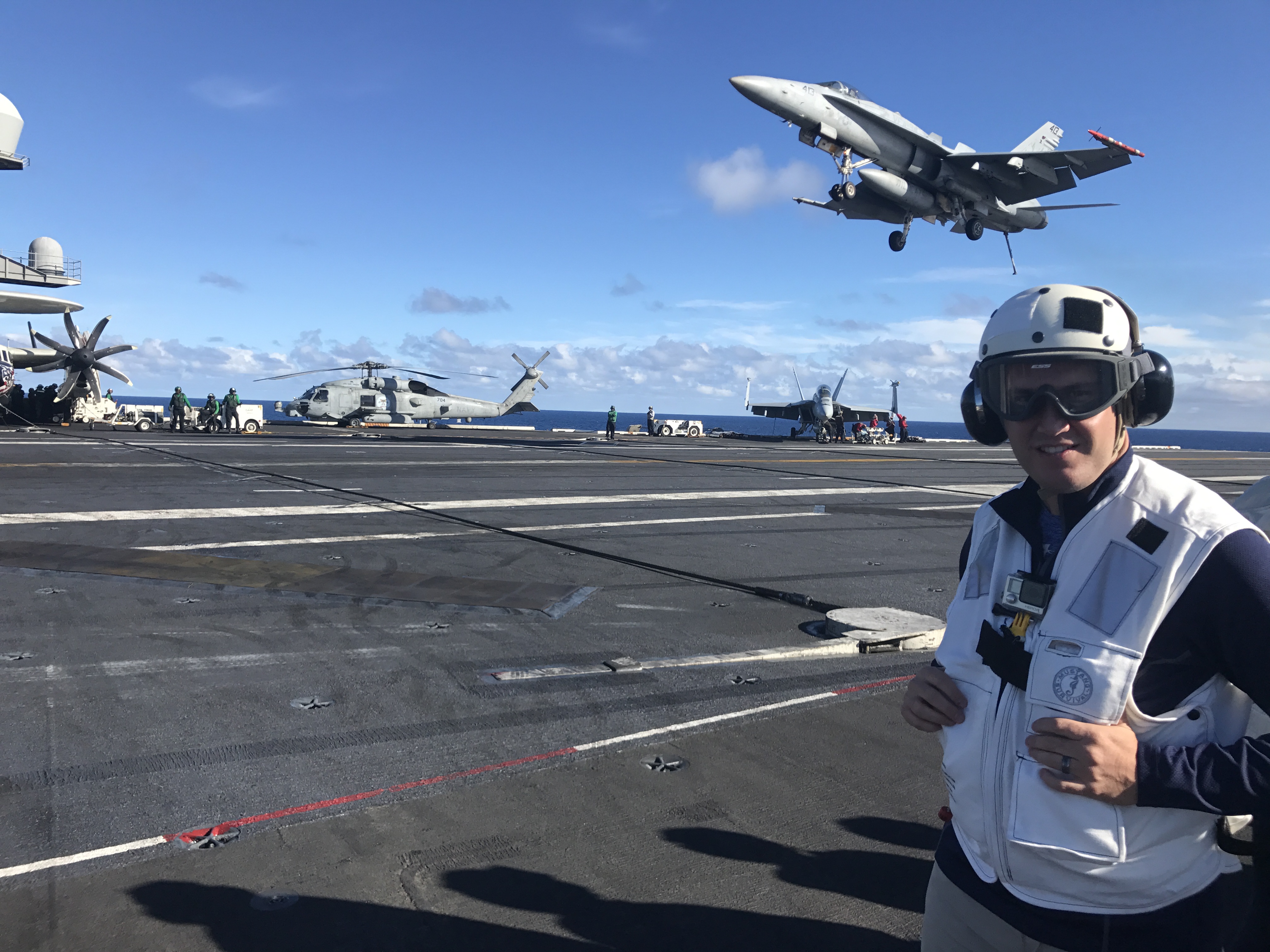 LTCC President Jeff DeFranco on the flight deck of the USS Carl Vinson, with an F-18 fighter jet landing behind him